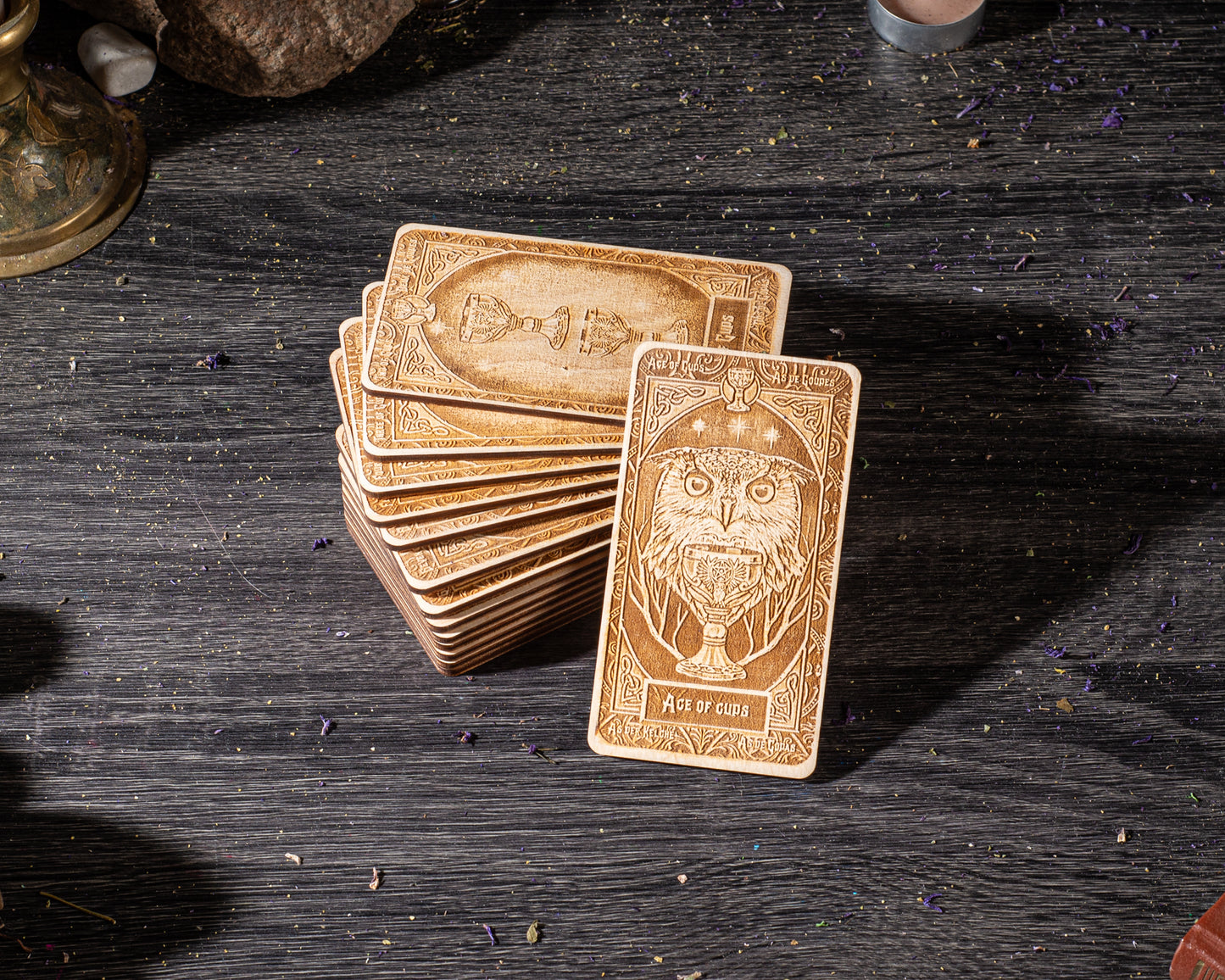 A stack of wooden tarot cards is displayed on a dark wooden surface, with a candle and some small objects in the background.