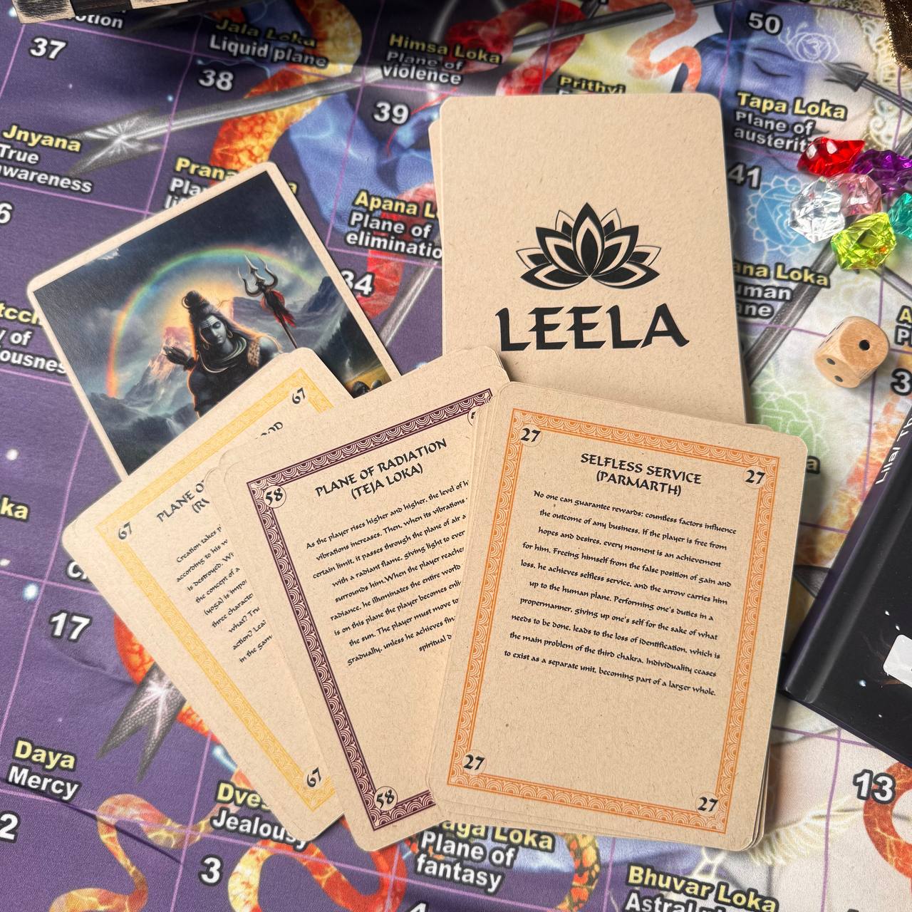 a collection of cards and game pieces, including a card with the word "LEELA" and a card with the word "SELFISH SERVICE (PARAMARTH)".