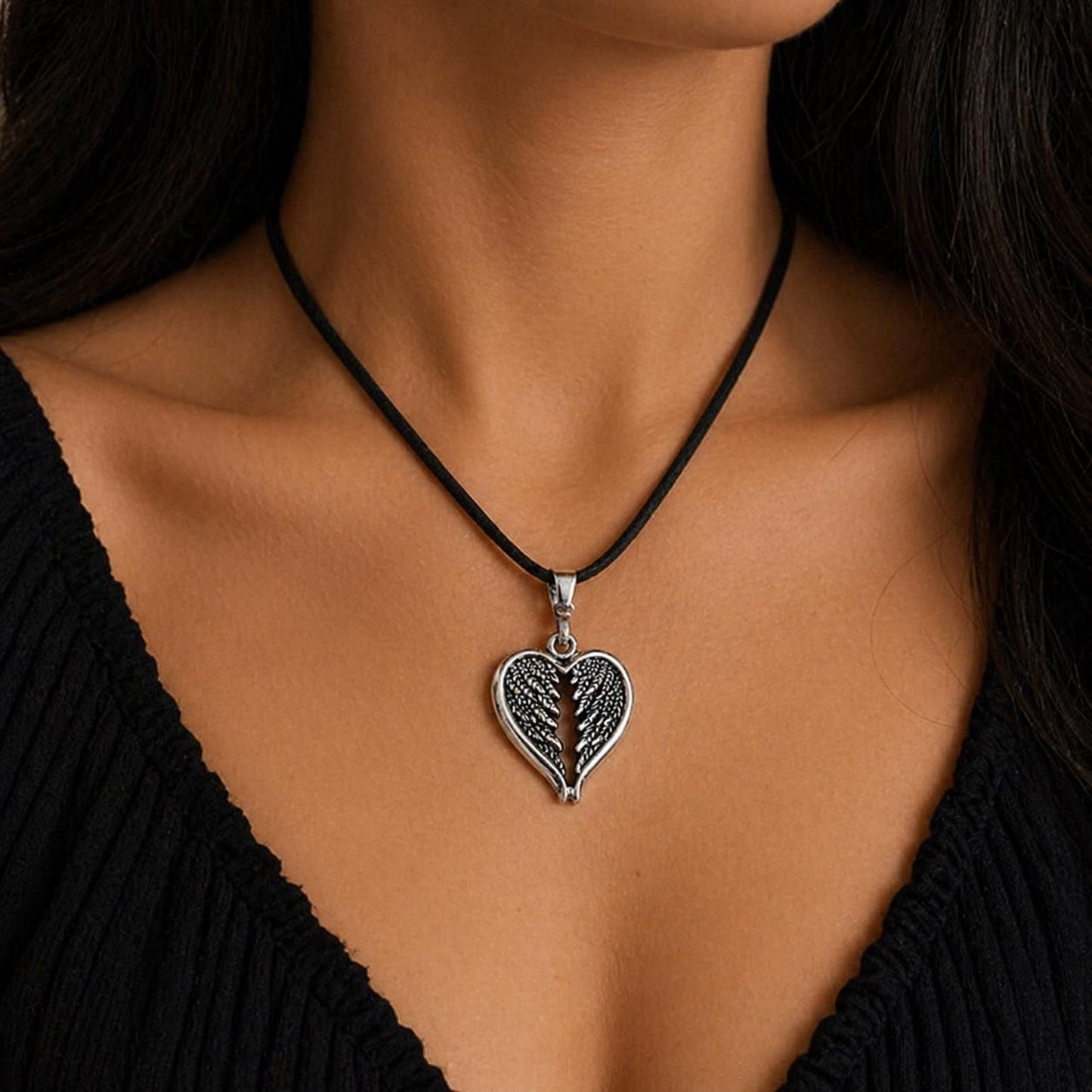 A silver heart-shaped pendant necklace with a black cord around the neck of a person wearing a black top.