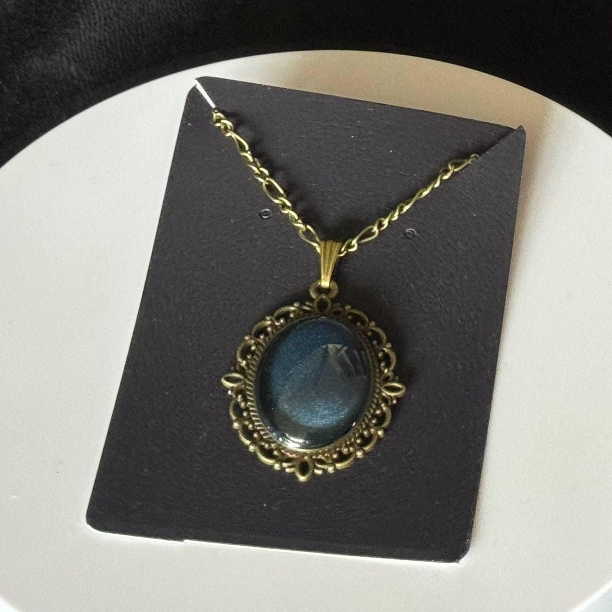 A necklace with a blue stone pendant is displayed on a black card.