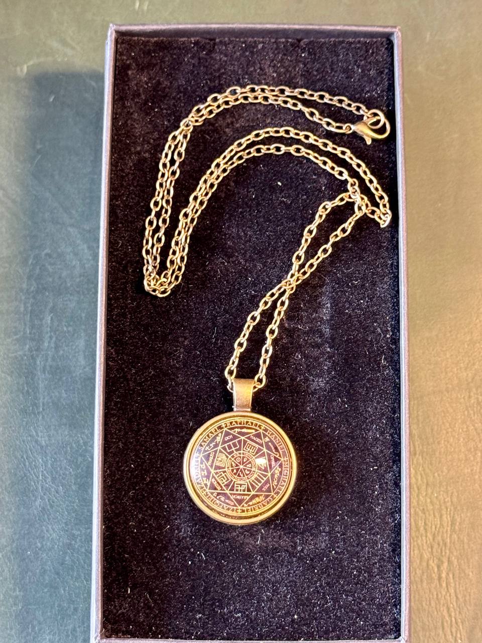 A gold-colored necklace with a circular pendant is displayed in a black jewelry box.