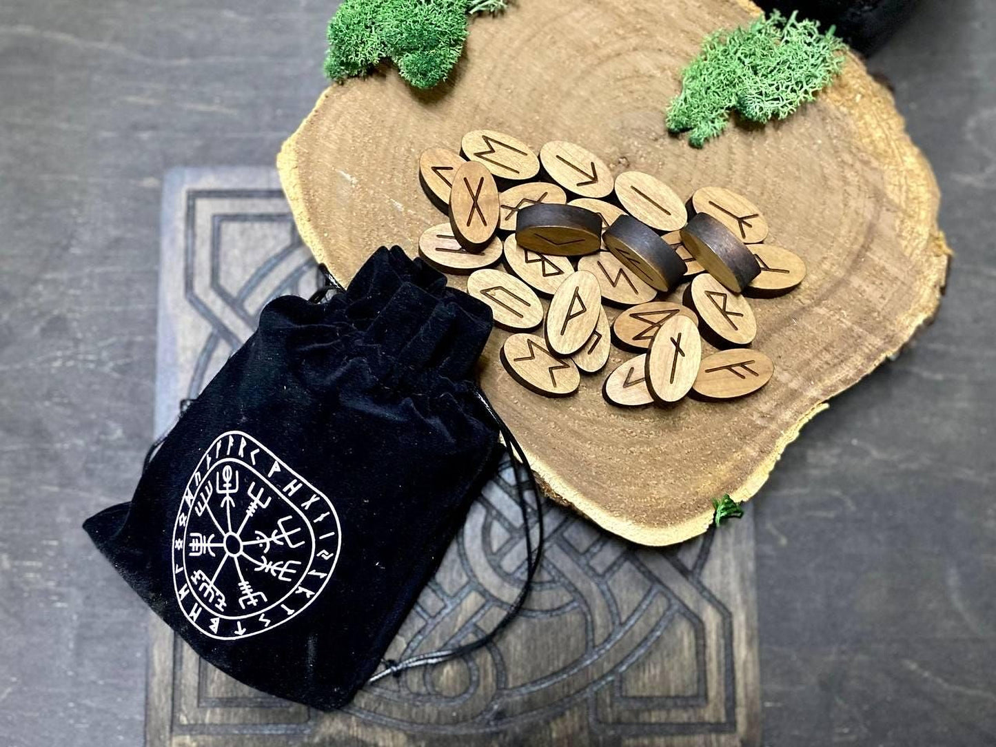a wooden board with a collection of wooden symbols, including what appear to be Viking symbols, and a black pouch with a white design on it, placed on a wooden surface.