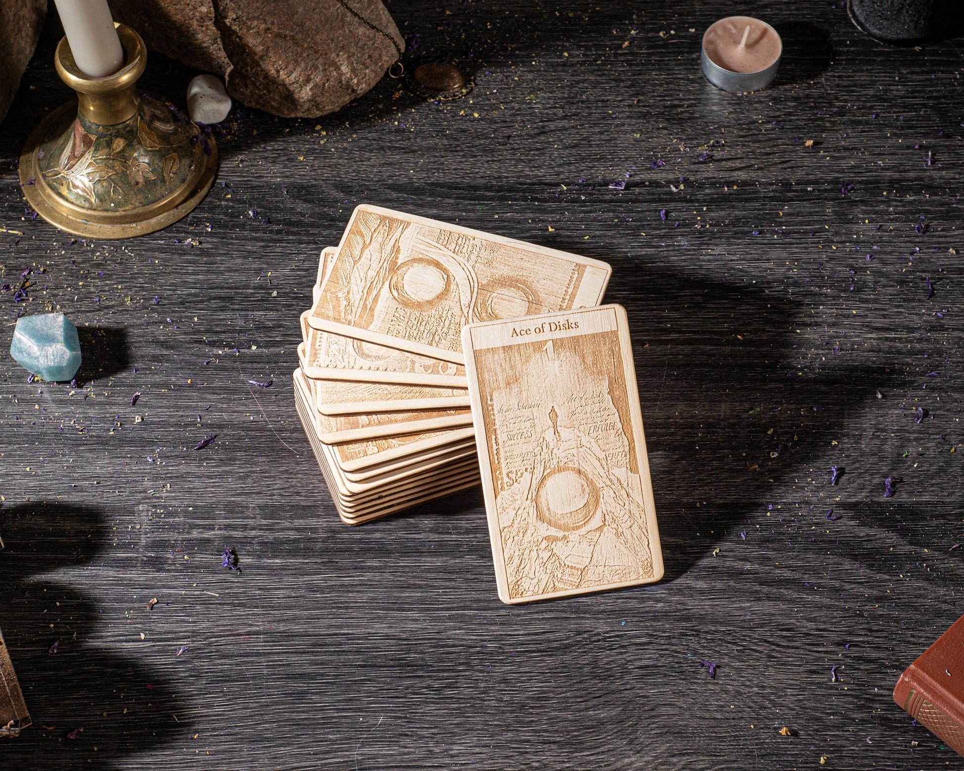 A deck of playing cards is displayed on a wooden surface, with a candle and various other objects in the background.