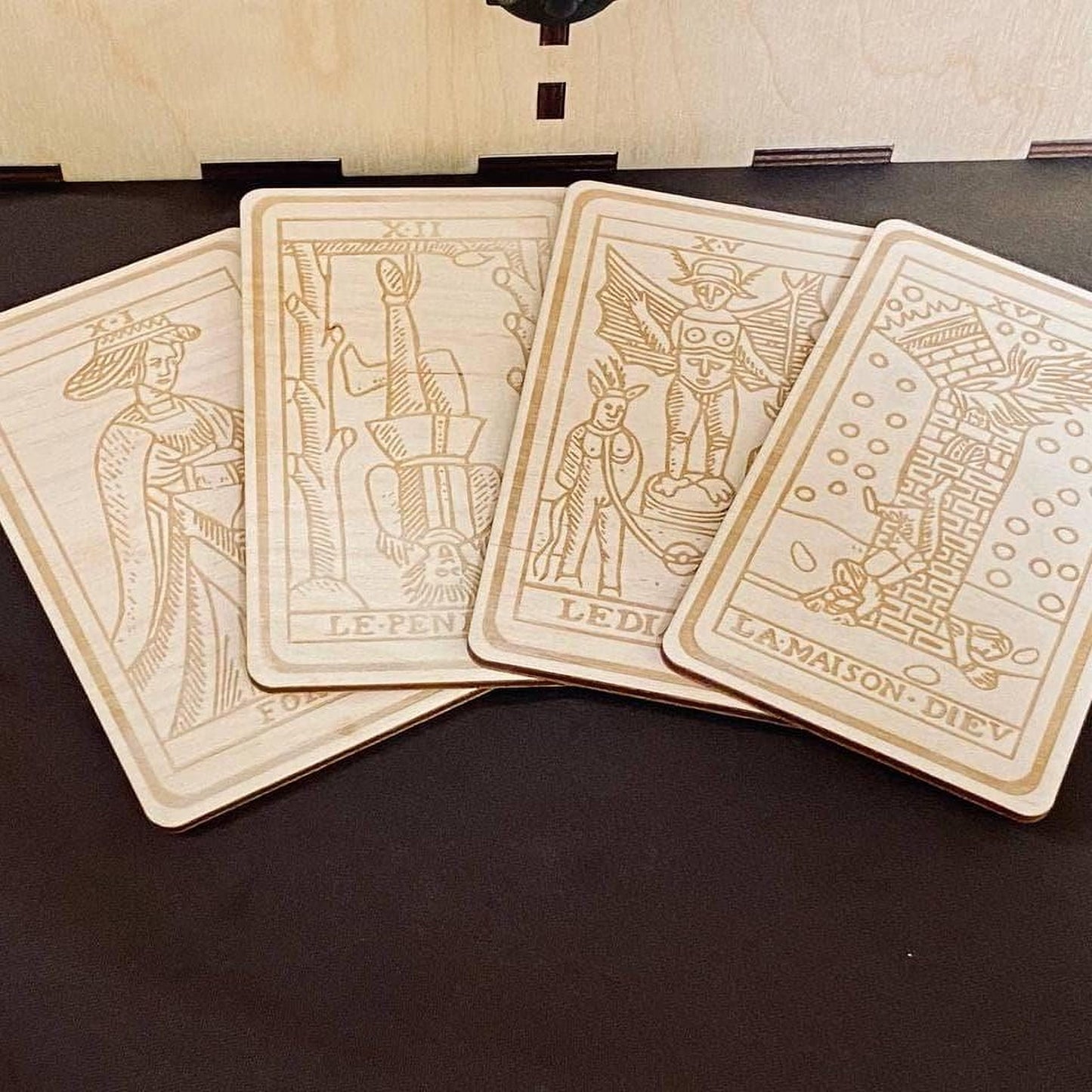 A collection of four wooden tarot cards with intricate designs and text, arranged in a fan-like formation on a dark surface.