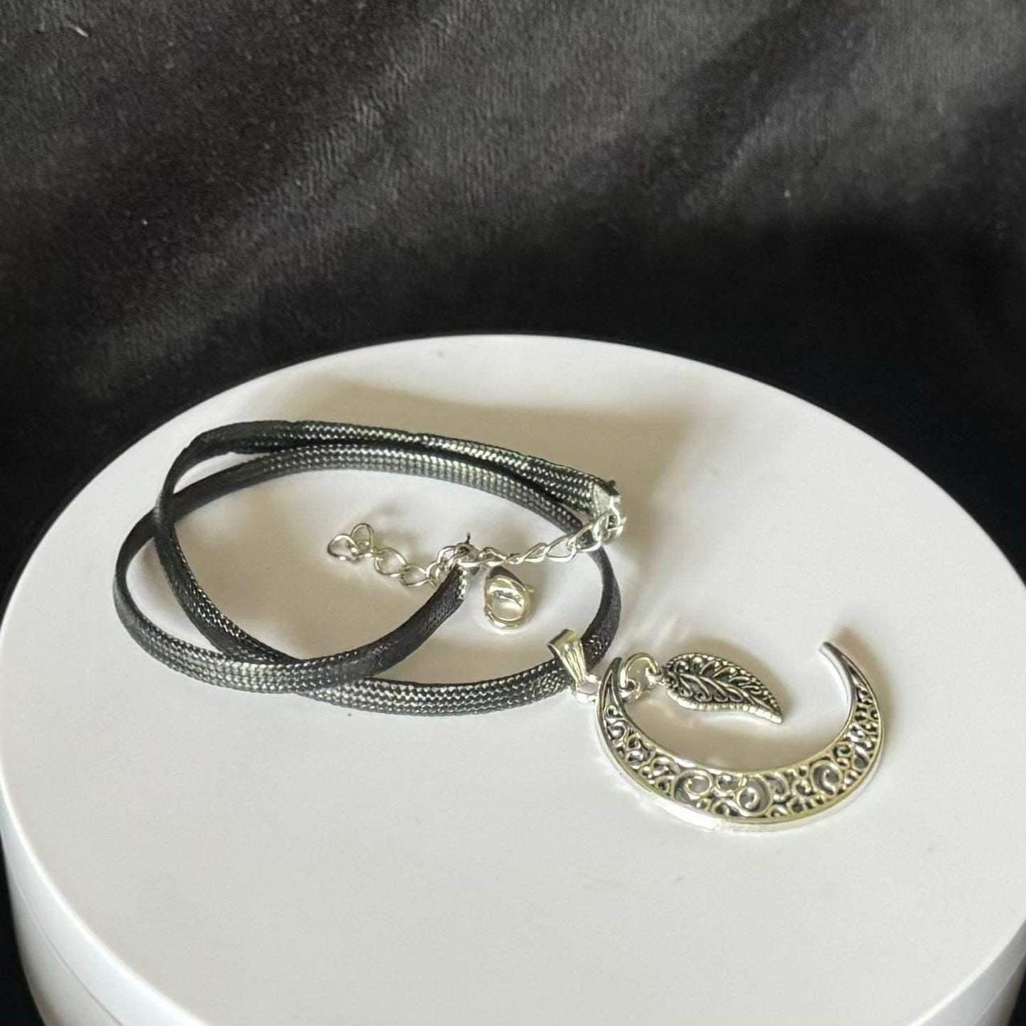 A silver necklace with a pendant featuring a crescent moon design and a leaf-like element.