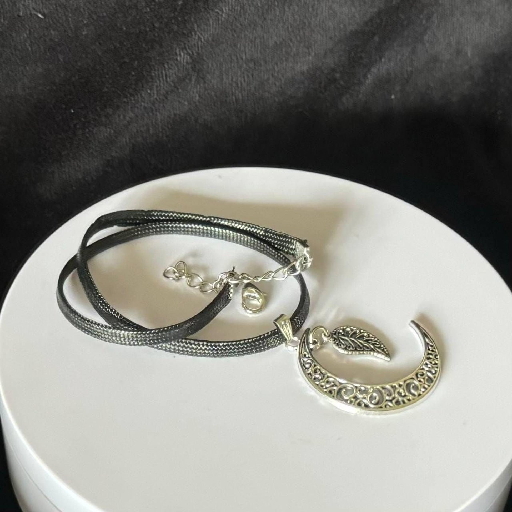 A silver necklace with a pendant featuring a crescent moon design and a leaf-like element.