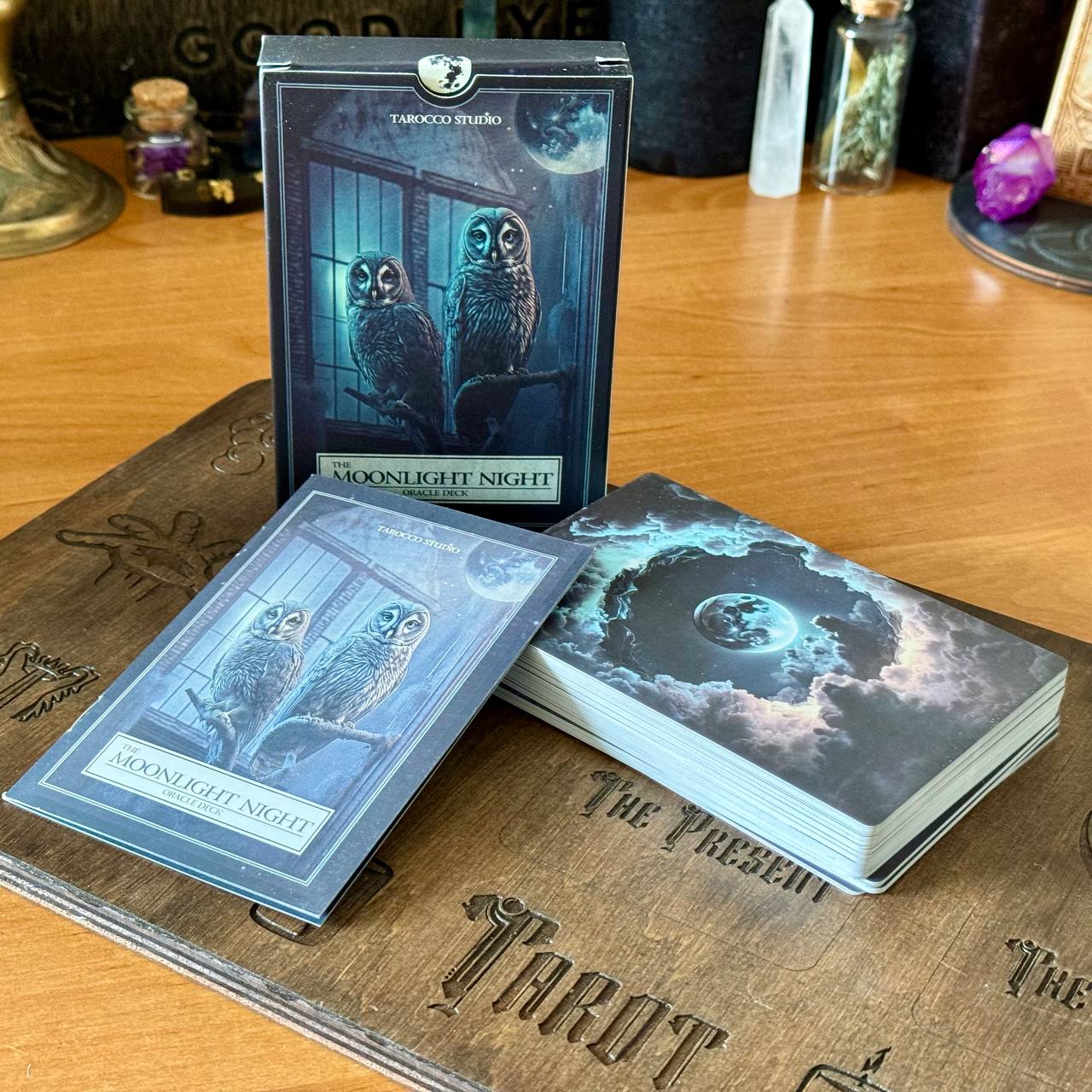 a tarot deck with a moonlit night theme, including a deck of cards and a box, all placed on a wooden surface.