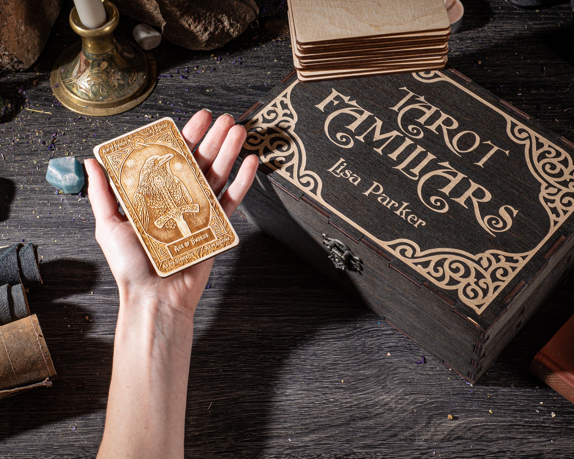 A hand holding a wooden tarot card with a dragon design, next to a wooden box with the title "Tarot Familiars" and the name "Lisa Parker" on it.