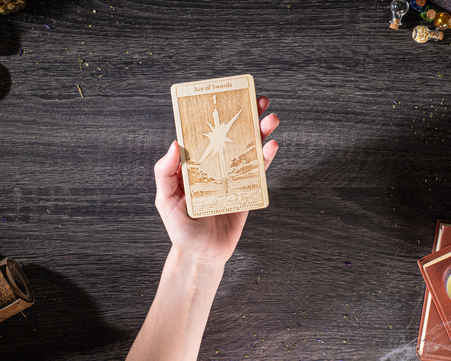 A hand holding a wooden tarot card with a star design on it, against a dark wooden background.