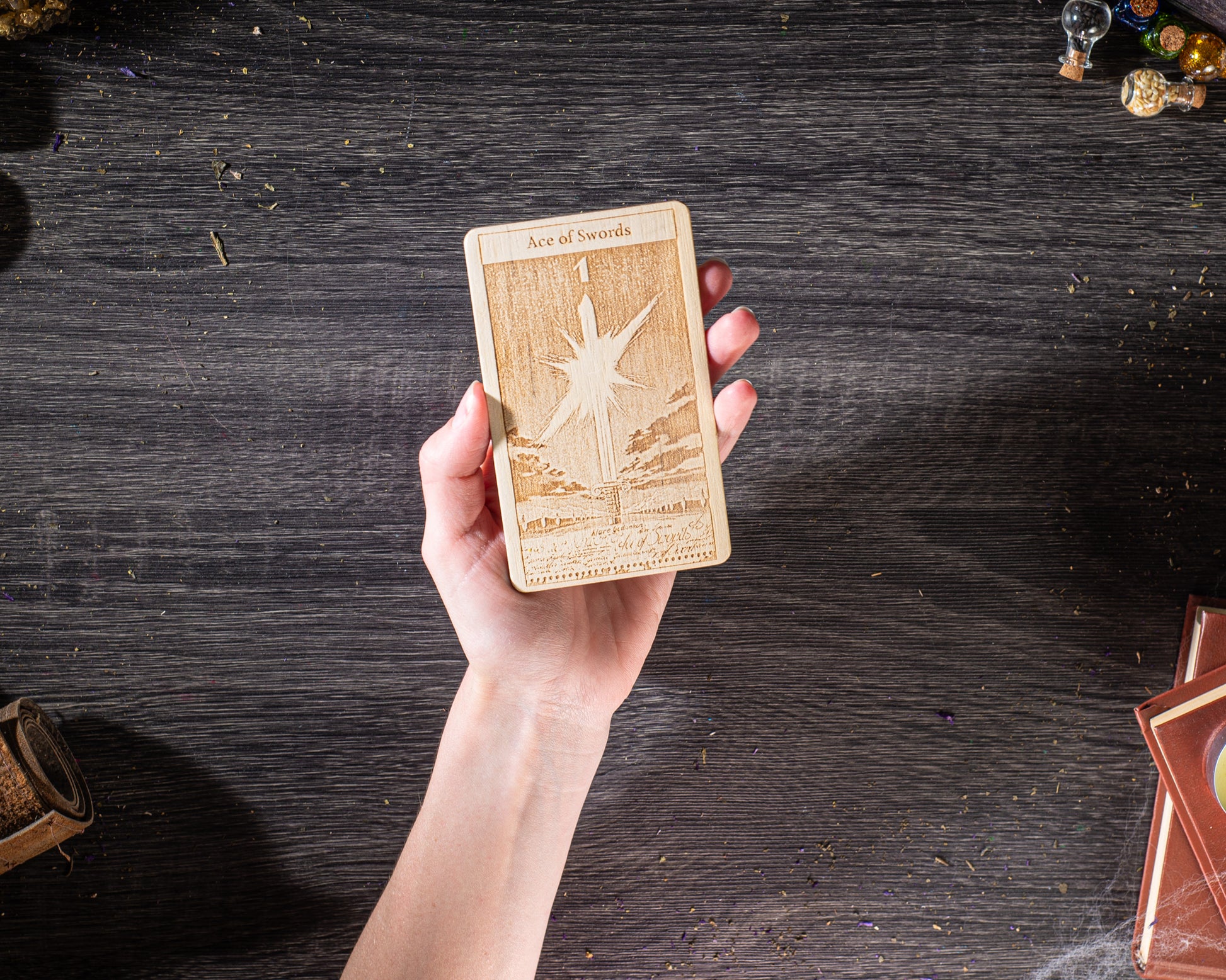 A hand holding a wooden tarot card with a star design on it, against a dark wooden background.