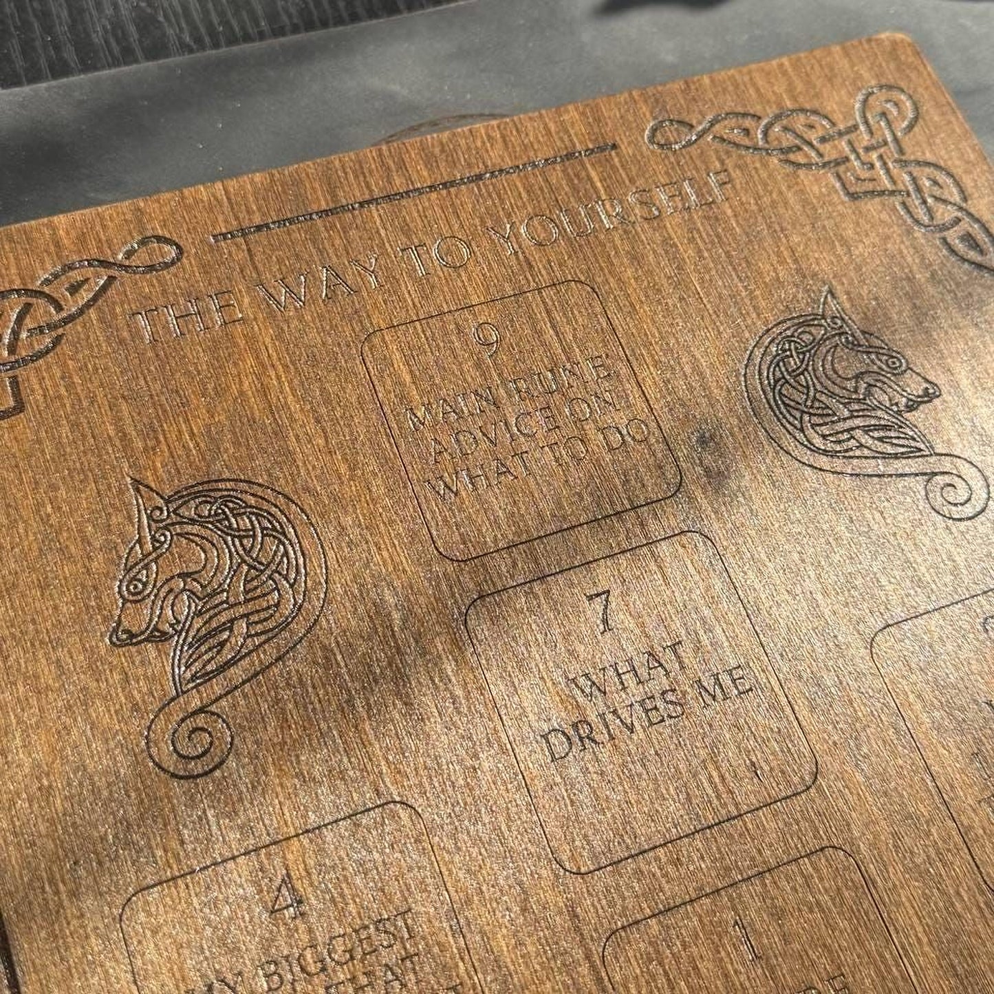 The image is a close-up of a wooden surface with embossed text and designs, including a wolf and a dragon.