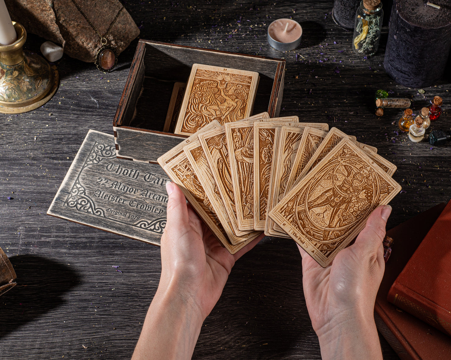 A pair of hands holding a deck of playing cards, with a wooden box and various other items on a dark wooden surface.