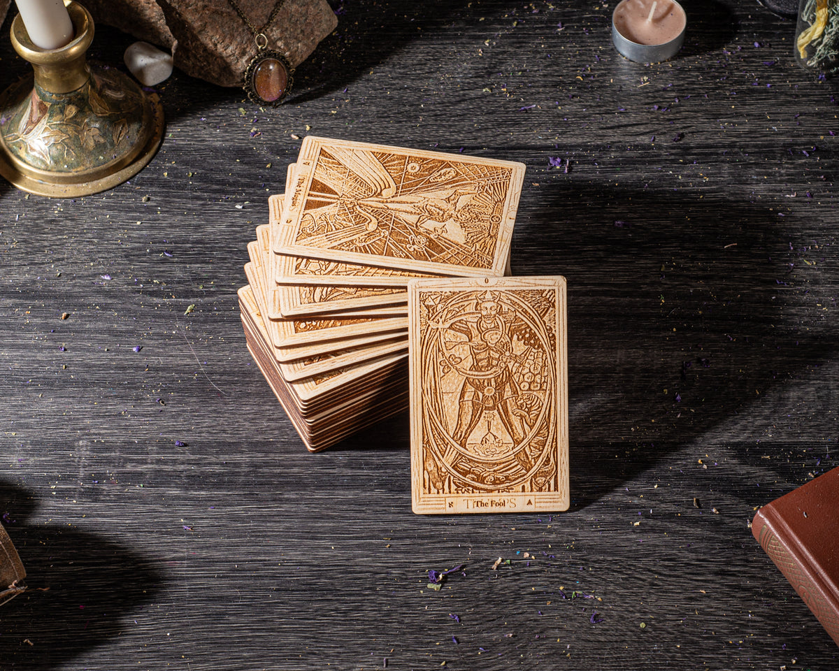A stack of wooden tarot cards is displayed on a dark wooden surface, with a candle and other objects in the background.