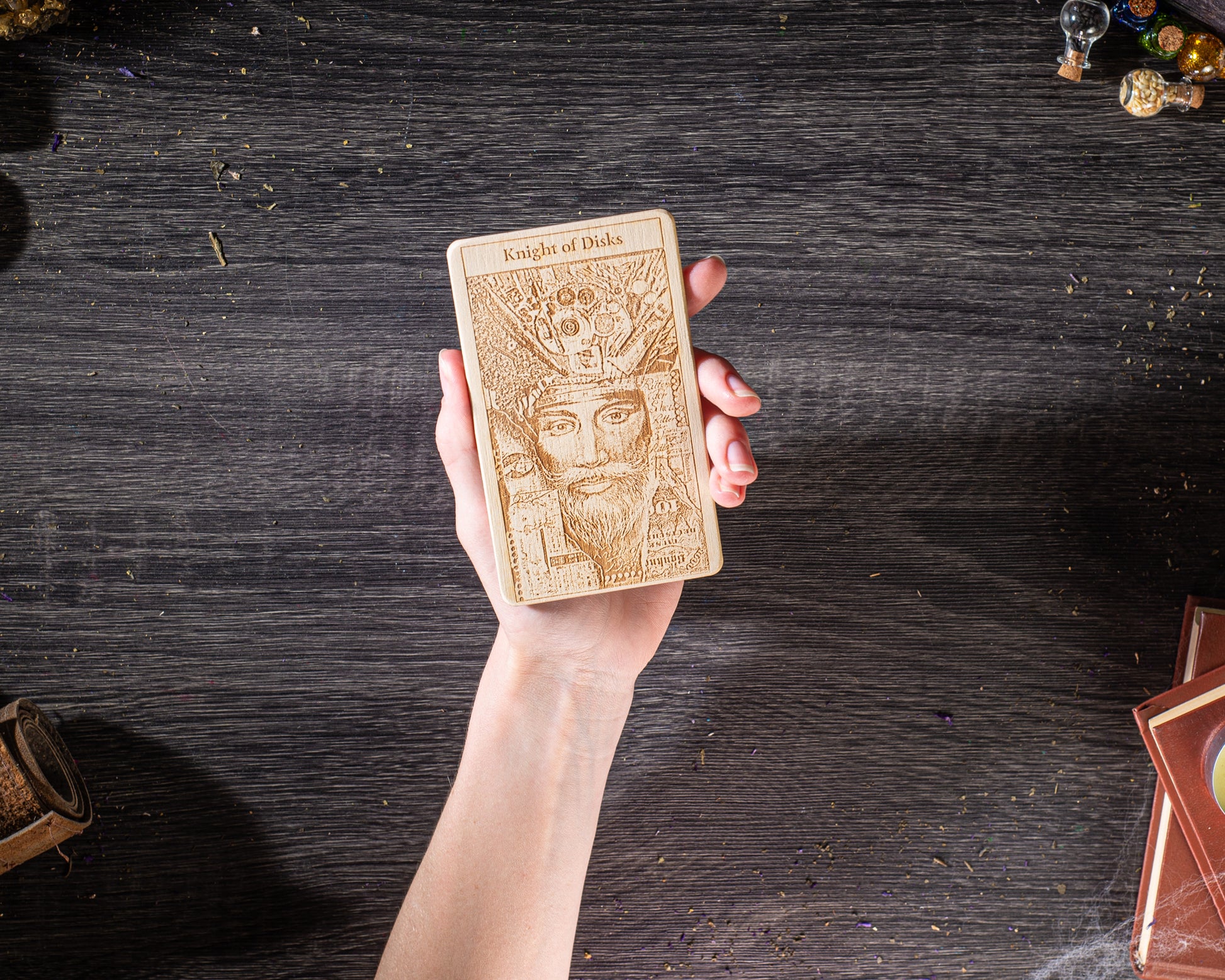 A hand holding a wooden card with an intricate design on it, placed on a wooden surface.