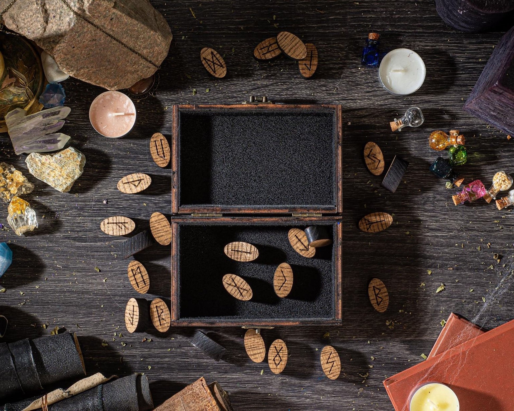 a wooden box with a black interior, surrounded by various objects such as crystals, candles, and other items on a dark wooden surface.