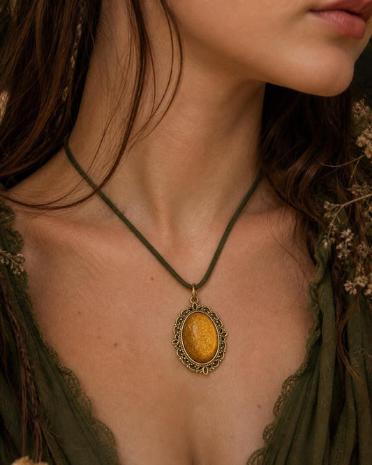 A close-up of a woman's neck and chest area, with a gold-colored pendant necklace featuring an oval-shaped pendant hanging from a green cord.