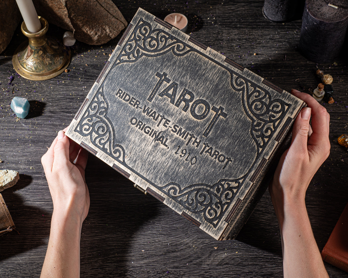 A person's hands holding a wooden box with a decorative border, which appears to be a tarot card box.