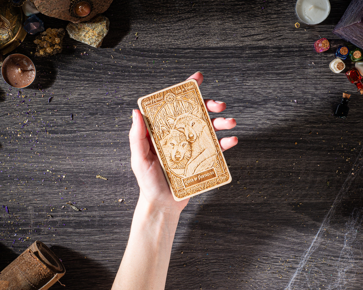 A hand holding a wooden object with a detailed design on it, placed on a wooden surface surrounded by various objects.